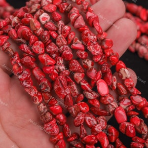 May include: A strand of red gemstone beads, with a speckled pattern, in a chip shape. The beads are strung on a clear thread and are approximately 10mm in length.