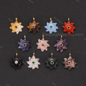 May include: A selection of gemstone pendants in a sunburst design. Each pendant features a different coloured stone, including yellow, brown, blue, red, purple, black, and pink. The pendants have gold-coloured bails and a central gemstone.