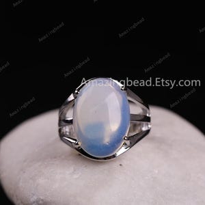 May include: A silver ring with a large oval-shaped opal gemstone. The opal is a milky white color with blue and white swirls.