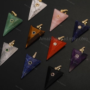 May include: A collection of ten triangular stone pendants in various colors including white marble, green, brown, pink, blue, red, purple, and black. Each pendant features a gold-tone metal bail and a small circular gemstone accent at the center.