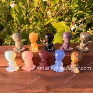 Peut inclure: Une collection de dix petites figurines d'extraterrestres sculptées à la main à partir de différents types de pierres précieuses polies. Les figurines sont toutes en position assise, les mains jointes devant elles. Les pierres précieuses comprennent l'améthyste, le quartz rose, le quartz clair, l'obsidienne et plus encore.