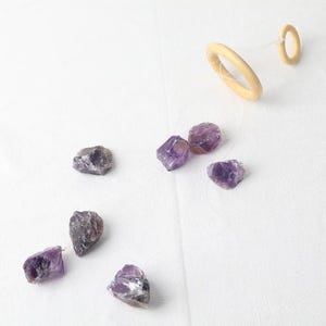 May include: A crystal wind chime with amethyst crystals hanging from wooden rings. The crystals are various shades of purple and are suspended from a clear string.