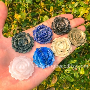 Peut inclure: Sept pendentifs en forme de rose sculptés en pierres précieuses de différentes couleurs, notamment bleu, blanc, noir et vert. Les roses sont présentées sur une main.