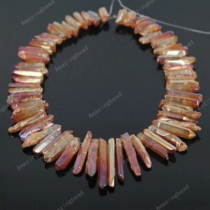 May include: A strand of orange and gold iridescent crystal point beads. The beads are faceted and have a pointed shape. The beads are strung on a clear thread.