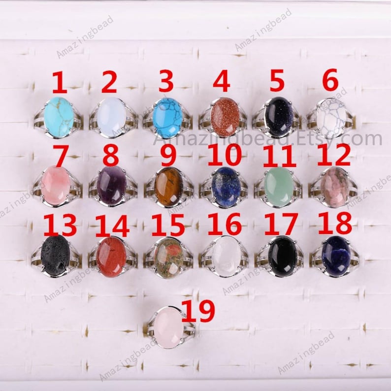 May include: A display of 19 silver rings with different colored oval-shaped gemstones. The rings are numbered 1 through 19.