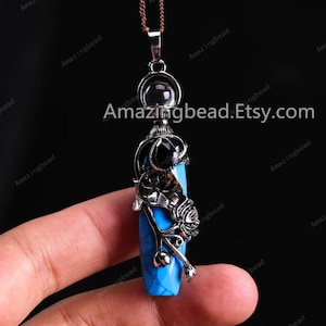 Pode incluir: Um colar com um pingente de prata adornado com uma pedra turquesa azul, uma pedra preta e um cristal transparente. O pingente tem a forma de uma garrafa com um design floral.