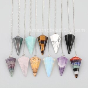 May include: A set of 10 crystal pendulums with silver chains. The pendulums are made of various crystals, including amethyst, rose quartz, tiger's eye, and clear quartz. Each pendulum is approximately 2 inches long.