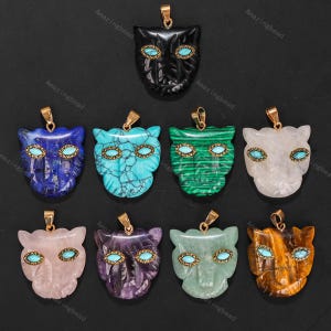 Puede incluir: Colección de colgantes de piedras preciosas con forma de cara de gato. Cada colgante presenta ojos turquesa y una fianza dorada. Los colgantes están hechos de varios materiales, incluyendo ónix negro, lapislázuli y malaquita.