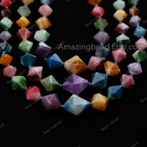 May include: A strand of colourful faceted gemstone beads. The beads are in a variety of shapes and sizes, and they are all strung together on a clear thread. The beads are a mix of green, blue, purple, red, orange, and yellow.
