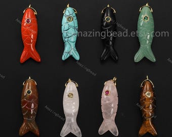 May include: A collection of eight carved fish pendants in various colors, including red, turquoise, black, and green. Each pendant has a gold-colored bail and a gemstone eye. The pendants are displayed against a black background.