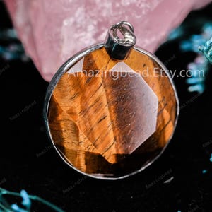 May include: A round pendant with a silver bail and a faceted tiger's eye stone. The stone is a deep brown with gold and black stripes. The pendant is approximately 1 inch in diameter.
