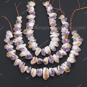 May include: Three strands of amethyst and citrine gemstone beads. The beads are faceted and have a natural, raw look. The beads are strung on thin orange thread.