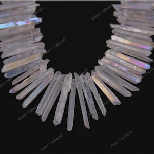 Può includere: Un filo di punte di cristallo di quarzo bianco iridescente, noto anche come quarzo aura di angelo, disposte a forma di ventaglio. Le punte misurano circa 2,5-5 cm di lunghezza.