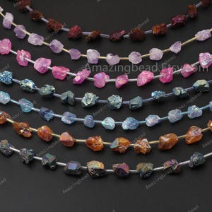 May include: A strand of iridescent, faceted, raw crystal beads in various colors, including pink, blue, orange, and black. The beads are strung on clear elastic thread.
