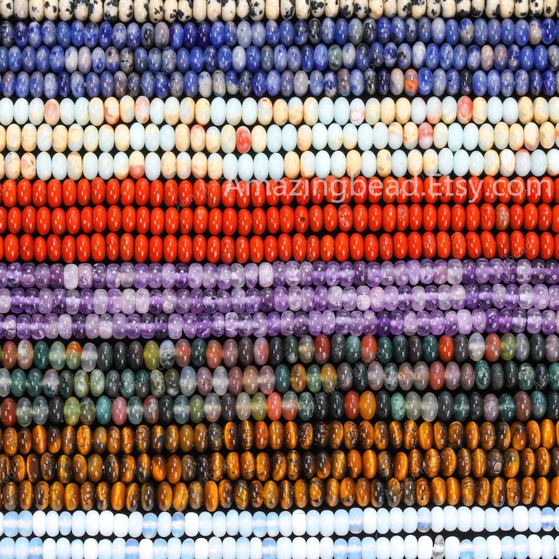 May include: A close-up of rows of gemstone beads in a variety of colours, including blue, white, red, purple, green, and brown. The beads are strung together, creating a textured pattern. The image features a variety of bead types and colours.