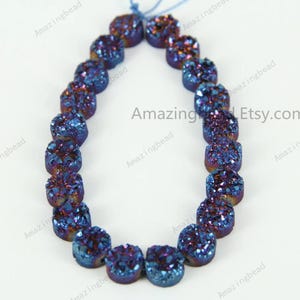 Puede incluir: Una hebra de cuentas de drusa azul y púrpura. Las cuentas son redondas y tienen una superficie texturizada. Las cuentas están enhebradas en un cordón delgado.