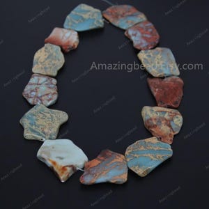 May include: A strand of irregularly shaped, flat, natural stone beads. The beads are a mix of brown, blue, and white with a marbled pattern. The beads are strung on a clear thread.