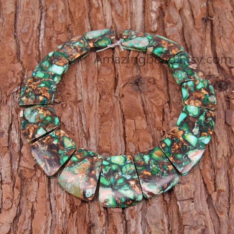K&ouml;nnte beinhalten: Eine Kette aus gr&uuml;nen und braunen Edelsteinperlen, jede Perle hat eine einzigartige, unregelm&auml;&szlig;ige Form mit einer facettierten Oberfl&auml;che. Die Perlen sind in einem Kreis auf einer Holzoberfl&auml;che angeordnet.