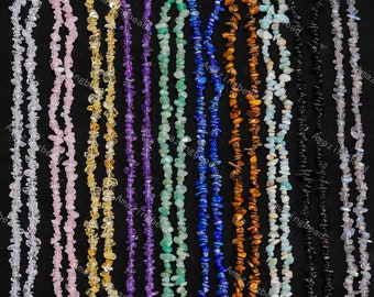 May include: A collection of 10 strands of chip gemstone necklaces in various colors, including clear, pink, yellow, purple, green, blue, brown, light blue, black, and gray. The necklaces are laid out in a row on a black surface.