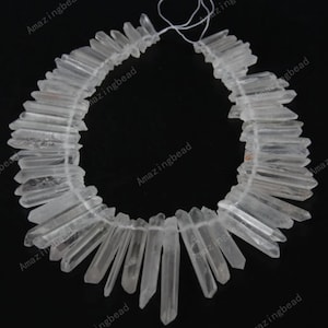 May include: A strand of clear quartz crystal points, also known as rock crystal, strung on a white thread. The points are various lengths and are arranged in a semi-circle shape.