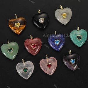 Puede incluir: Una colección de colgantes de piedras preciosas en forma de corazón en varios colores, incluyendo ojo de tigre, ónix negro y cuarzo rosa. Cada colgante presenta una pequeña piedra preciosa contrastante engastada en un marco de metal dorado, con un lazo dorado para colgar.