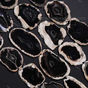 May include: A collection of polished agate slices, each with a unique pattern. The slices are primarily black with white and cream-colored banding around the edges. The natural stone pieces vary in shape and size, creating a visually interesting display.