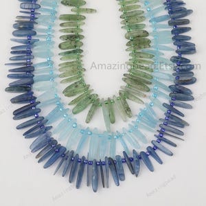 May include: Three strands of gemstone beads, each strand featuring a different colour: blue, light blue, and green. The beads are long and narrow, resembling small, pointed sticks. The beads are strung on a clear thread.