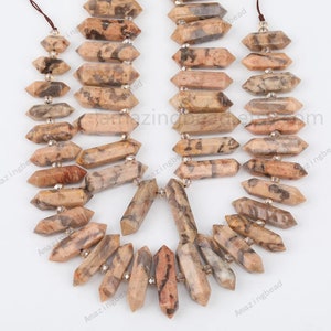 Könnte beinhalten: Eine Strähne aus braunen und weißen Edelsteinperlen mit einer facettierten, spitzen Form. Die Perlen sind auf einer durchsichtigen Schnur mit kleinen silbernen Abstandshaltern zwischen jeder Perle aufgefädelt.