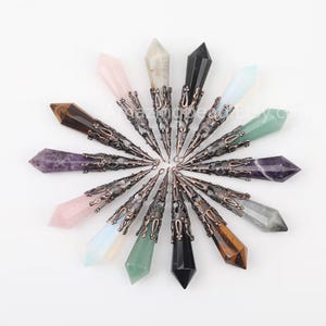 Puede incluir: Una colección de 14 colgantes de cristal de punta con engastes metálicos ornamentados. Los cristales son de varios colores, incluyendo amatista, cuarzo rosa, cuarzo transparente, ojo de tigre y aventurina verde.