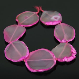 May include: A strand of pink agate beads with a clear center and a pink edge. The beads are oval shaped and have a natural, irregular shape.