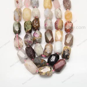 Puede incluir: Una hebra de cuentas de piedras preciosas facetadas multicolores. Las cuentas son una mezcla de rosa, verde, marrón, blanco y negro. Las cuentas son todas de aproximadamente el mismo tamaño y forma, y están enhebradas en un hilo rosa.