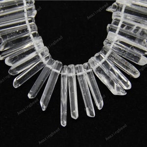 May include: A strand of clear quartz crystal beads, each bead is a long, thin, and pointed crystal. The beads are arranged in a fan shape, with the points of the crystals facing outwards.