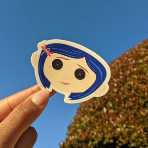 May include: A sticker featuring a cartoon illustration of a girl with blue hair and large, button-like eyes. She is wearing a red dragonfly in her hair. The sticker has a white background and the text "@grantyourwish" is printed at the bottom.