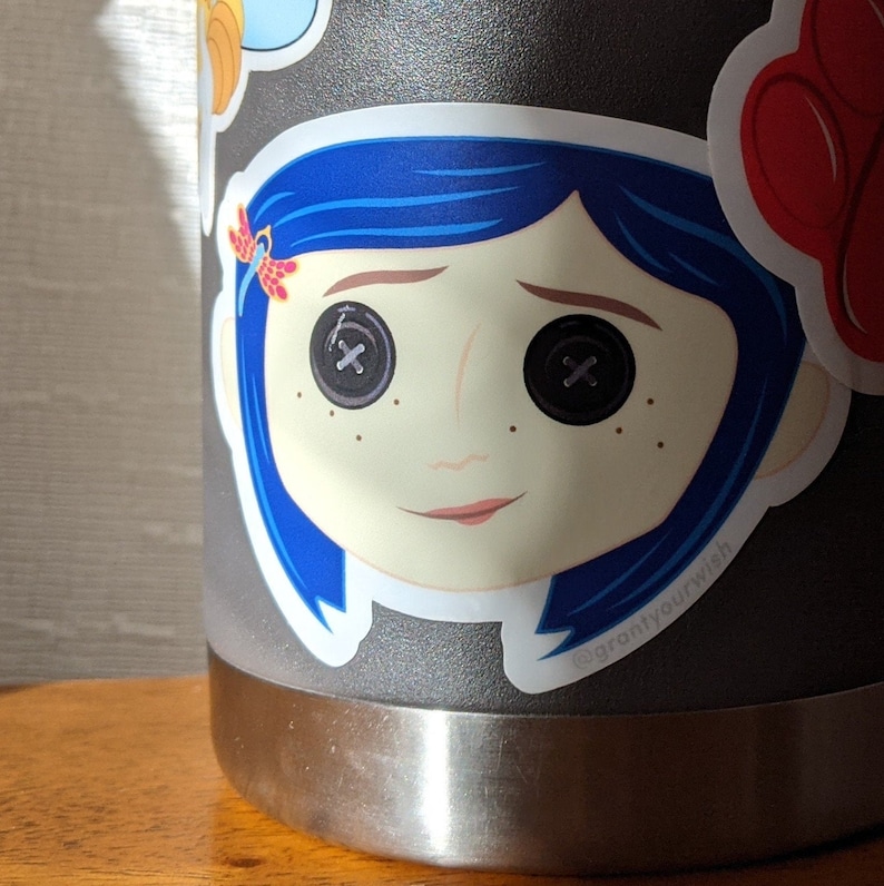 May include: A sticker of a cartoon girl with blue hair and big button eyes. The sticker is on a gray metal water bottle. The sticker has the text "@grantlyourwish" on the bottom.