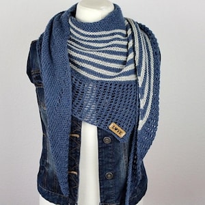 May include: A blue knit shawl with a striped pattern in white and blue. The shawl is draped over a denim jacket. A small wooden tag with the word "LOVE" is attached to the shawl.