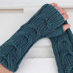 Può includere: Guanti senza dita lavorati a maglia color teal con un motivo a trecce. I guanti sono realizzati in un filato morbido e strutturato. Il motivo a trecce aggiunge un elemento decorativo. Un accessorio invernale.