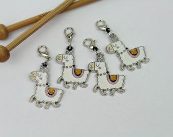 May include: Four silver llama stitch markers with black cords. Each llama is white with a pink and yellow saddle and black eyes.