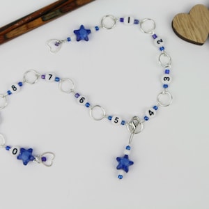 Könnte beinhalten: Zwei Sätze blauer und weißer Perlenketten mit silbernen Sprungringen und blauen Sternanhängern. Die Ketten sind von 0 bis 9 und von 1 bis 7 nummeriert.