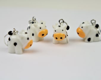 May include: Four white cow charms with black spots and orange noses. The charms are hanging from silver loops.