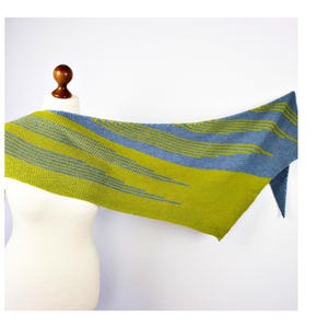 Könnte beinhalten: Ein dreieckiges Stricktuch mit einem Color-Block-Design in leuchtendem Limettengrün und gedämpftem Schieferblau. Der Stoff zeigt ein strukturiertes Kraus-Rechts-Strickmuster mit abwechselnden horizontalen Streifen und einfarbigen Bereichen.