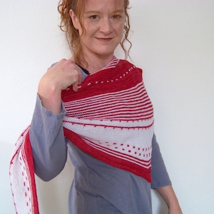 Puede incluir: Un chal triangular de rayas rojas y blancas con un patrón de puntos. El chal está hecho de tejido de punto y lo lleva una persona con el pelo rojo.