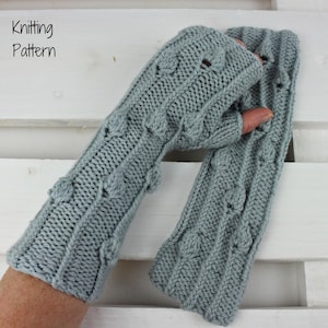 May include: A pair of light gray knitted fingerless gloves with a cable knit design and leaf-shaped accents. The text "Knitting Pattern" is in the upper left corner. The gloves are displayed on a white wooden surface.
