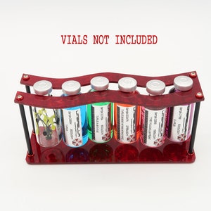 May include: Red acrylic stand with six clear glass vials, each containing a different colored liquid and labeled with "Umbrella Corp." and a description. The text "VIALS NOT INCLUDED" is printed above the stand.
