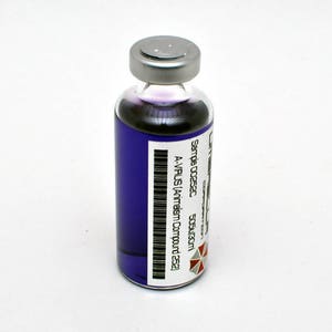 Peut inclure: Une petite fiole en verre avec un bouchon argenté remplie d'un liquide violet. La fiole porte une étiquette blanche avec du texte noir qui indique "Sample 00252C A-VIRUS (Antiserum Compound 252)" et un code-barres. L'étiquette comporte également un symbole rouge et blanc.
