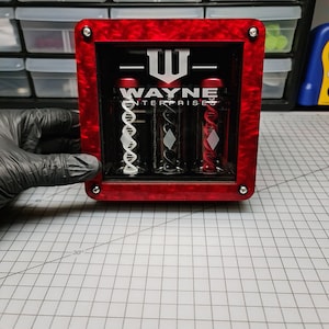 May include: A red, clear acrylic display case with a black and white Wayne Enterprises logo. The case contains three clear tubes with black, white, and red contents.