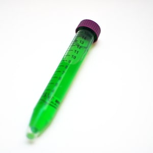 Puede incluir: Un tubo de ensayo de vidrio transparente con una tapa morada lleno de líquido verde. El tubo tiene marcas para medir el volumen en mililitros.