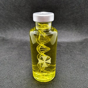 Könnte beinhalten: Eine klare Glasflasche mit einem silbernen Verschluss, die eine gelbe Flüssigkeit mit einem spiralförmigen Objekt enthält. Die Flasche hat ein weißes Emblem mit einem Kreuz mit vier Spitzen.