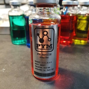 Puede incluir: Un vial de vidrio transparente con una tapa plateada y una etiqueta que dice "PYM TECHNOLOGIES PYM PARTICLE 400mg/30ml". El vial contiene un líquido rojo. Otros viales con líquidos de colores están en el fondo.
