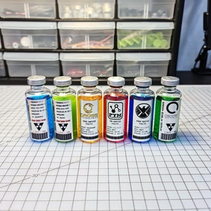 May include: Seven small glass bottles containing colourful liquids and labels. The labels feature various logos and text, including "Pym Particles", "Cross Technologies", and "Oscorp".