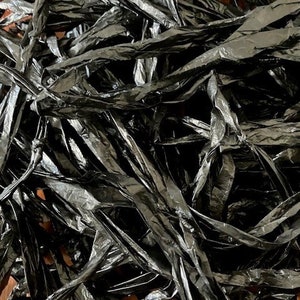 May include: A close-up of a pile of shiny, black, ribbon-like material. The material is crumpled and layered, creating a textured and reflective surface. The ribbons appear to be made of a plastic or similar material.